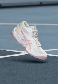 Λευκό και ροζ αθλητικό παπούτσι κρεμασμένο πάνω από μια μπλε γήπεδο τένις με λευκές γραμμές ορίων.