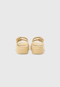 Yellow rubber sandals with a textured surface, two adjustable straps, and a chunky sole. Rear view, featuring smooth lines and minimal detail.