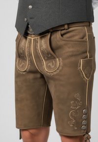 Pantaloni court in pelle marrone con ricami decorativi, tasche accentuate e bottoni argentati. Materiale testurizzato, vestibilità su misura e design fino al ginocchio.