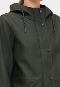 Ciemnozielona wodoodporna kurtka z kapturem, zatrzaskami i regulowanymi sznurkami. Gładka faktura o zwartej konstrukcji.