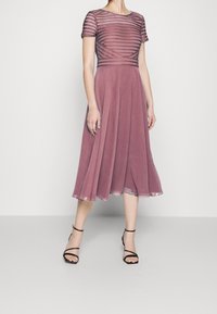 Mauve Kleid mit einem taillierten, gestreiften Oberteil und einem fließenden Rock. Durchsichtiger Stoff oben, knielang, kombiniert mit schwarzen Riemchenabsätzen.