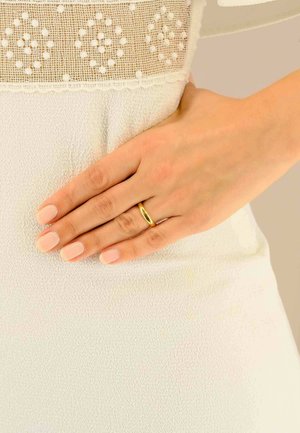 Goldring an einer Hand mit hellrosa Nägeln, die auf einem strukturierten weißen Stoff ruht. Der Ring hat eine glatte, ovale Form und einen polierten Finish.