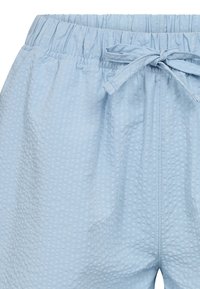 Light blue shorts made from textured material. Features an elastic waistband with a drawstring tie and subtle pattern.