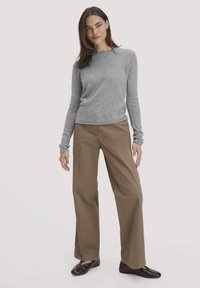 Grau langärmliger Pullover mit rundem Ausschnitt, kombiniert mit lockeren, braunen Hosen und dunkelbraunen Schuhen. Glatte Textur, lässige Passform.