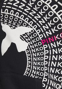 Tissu noir avec le texte blanc "PINKO" répété en motif circulaire, une grande silhouette d'oiseau blanche, et un "PINKO" en rose.