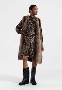 Abito a stampa leopardo con gilet di pelliccia, stivali in pelle neri fino al ginocchio e grandi orecchini a cerchio d'oro. Presenta una chiusura a papillon e un orlo svasato.