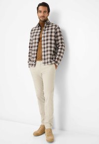 Geruite button-up shirt in bruin, crème en marine, gecombineerd met een bruine coltrui en beige corduroy broek; tan suède schoenen maken de outfit compleet.