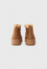 Bottines en suède marron avec un doux doublure en fourrure au col, dotées d'une épaisse semelle en caoutchouc et d'une fermeture éclair sur le côté pour un enfilage facile.