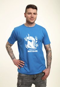 Camiseta de algodón azul con un estampado gráfico blanco de una figura sentada y el texto "MATISSE" debajo, con una textura suave y cuello redondo.
