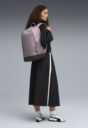 Purple backpack with a textured finish and a black base. Features adjustable straps and a prominent logo. Worn by a person in a black outfit.