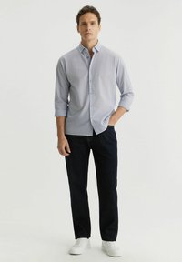 Jasnoniebieska w paski koszula z guzikami z podkręconymi rękawami, w zestawie z ciemnoniebieskimi dżinsami i białymi sneakersami. Prosty design z klasycznym krojem.