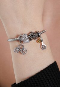 Silver charm bracelet features charms of a bicycle, windmill, ladybug, and tennis racket, showcasing intricate detailing and a smooth metal finish.