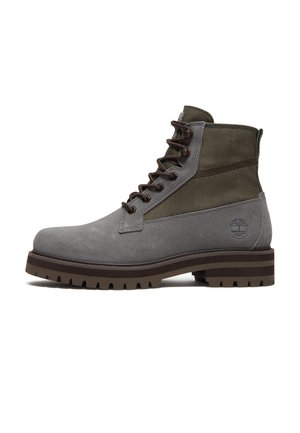 Bota de tacón corto de ante gris y tela verde oliva con cordones, suela marrón resistente y logo de árbol en relieve en el talón.