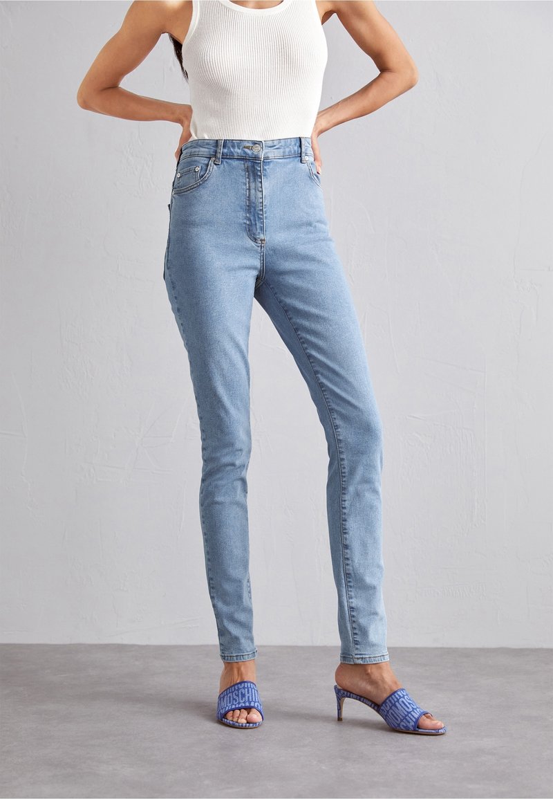 Jeans blu chiaro a vita alta, slim fit, realizzati in denim. Abbinati a tacchi aperti blu con motivo. Il top del modello è un canotta bianca a coste.