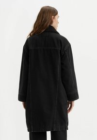 Giubbotto in denim nero con una vestibilità rilassata, caratterizzato da un colletto in shearling nero testurizzato, maniche larghe e dettagli di cucitura in vista.