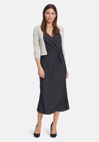 Fekete csipkeborítású ruha selymes felülettel, V-nyakkivágással és derékmegkötővel, világosszürke rövid kardigánnal párosítva.