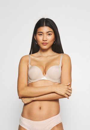 Nude push-up bra with smooth, molded cups, adjustable straps, and a v-shaped center. Paired with light pink panties featuring a logo.