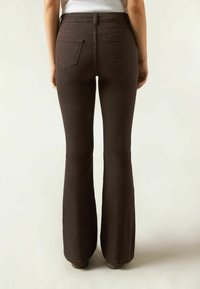 Pantalons évasés marron avec une texture lisse, comportant deux poches arrière et une taille haute, se rétrécissant vers un ourlet plus large au niveau des chevilles.