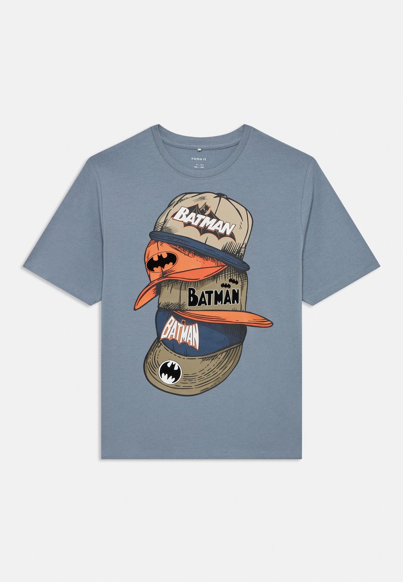Zila kokvilnas T-krekls ar grafiku, kurā attēloti sakrauti cepures ar tekstu "BATMAN", dažādu stilu un krāsu cepurēm, tostarp oranžiem un bēšiem akcentiem.