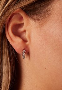 Zilveren oorringen met een spiraalontwerp, voorzien van kleine heldere edelstenen in een rij. Gelaagd oppervlak, dicht bij het oor.