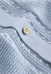 Tissu tricoté bleu clair avec des points blancs et un bouton beige à quatre trous cousu au centre.