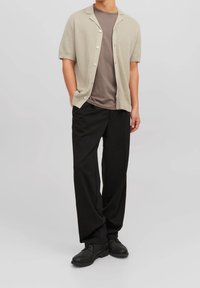 Cardigan corto a maniche corte di colore beige chiaro sopra una maglia grigia, abbinato a pantaloni neri larghi e scarpe nere; tessuti lisci e testurizzati.