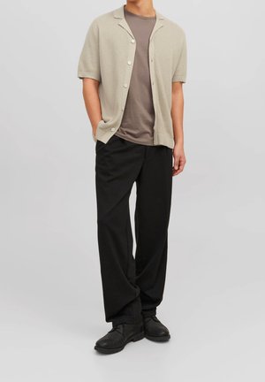 Jasno beżowy kardigan na krótki rękawek noszony na szarym T-shircie, w połączeniu z luźnymi czarnymi spodniami i czarnymi butami; gładkie i teksturowane tkaniny.