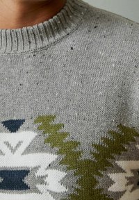 Maglione grigio con scollo a coste, caratterizzato da una spessa trama a maglia. Motivi evidenti in bianco, blu navy e verde, inclusi disegni geometrici.