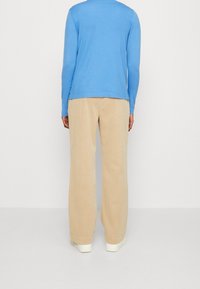 Ljusblå långärmad tröja, kombinerad med beige vida byxor, båda i mjuka material, med enkla, rena linjer och en avslappnad design.