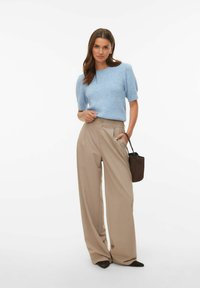 Pull en tricot bleu clair à manches courtes associé à un pantalon beige à jambes larges. La tenue comprend un petit sac à main marron et des chaussures noires à bouts pointus.