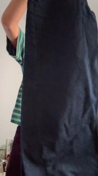 Oseba v zeleni prugasti srajci drži temno modre hlače, s čimer delno zakriva svoj trup in roko.