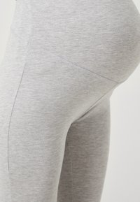 Sive leggins, narejeni iz mehkega, raztegljivega blaga; imajo preprost dizajn z gladko teksturo in brez vidnih vzorcev ali kovinskih delov.