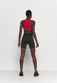 Red athletic crop top with textured pattern and keyhole back, paired with black shorts featuring orange accents. Athletic shoes worn.