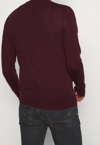 Bordeauxroter Strickpullover mit langen Ärmeln und Rundhalsausschnitt, ausgestattet mit gerippten Bündchen und Saum. Glatte Textur mit einer taillierten Silhouette.