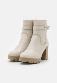 Stivaletti alla caviglia in finta pelle beige con chiusura a zip, tacco largo e suola in gomma con un motivo testurizzato. Dettaglio con cinturino regolabile.