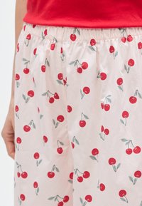 Pantalon de pyjama en coton avec une ceinture élastique, présentant un fond rose et un motif répétitif de cerises en rouge et vert.