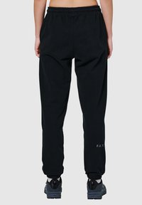Schwarze Jogginghosen mit elastischem Bund, schmalen Beinabschlüssen und einem kleinen aufgedruckten Logo "F.U.T." in der Nähe des Knöchels. Hergestellt aus weichem Stoff.