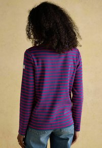 Tumedast ja roosast triibuline pikkade varrukatega särg, millel on ümmargune kaelus ja lihtne disain. Pehme kangas siledaga tekstuuriga.