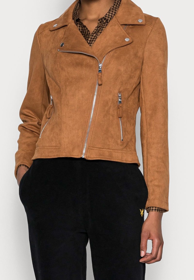 Veste de motard en faux suède marron avec des zippers argentés, des boutons-pression et des poches latérales. Présente un design ajusté et un col avec des revers.