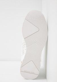 Semelle de basket blanche avec caoutchouc texturé, motifs géométriques, et détail de marque "MICHAEL KORS" embossé sur le côté.