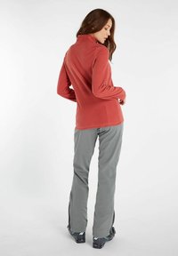 Fleece pullover i koral med høj krave, parret med grå bukser med lynlåse i kanten og en strømlinet pasform. Glat tekstur hele vejen igennem.