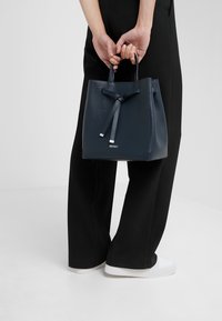 Borsa a secchiello in pelle blu navy con finitura testurizzata, caratterizzata da un dettaglio a nastro e accessori in argento. Logo impresso sulla parte anteriore.