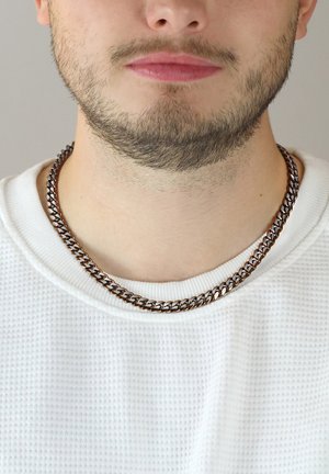 Silberfarbener Metallkettenhalsreifen mit ineinandergreifenden Gliedern, der auf einem strukturierten weißen Rundhalsausschnitt-Pullover liegt.