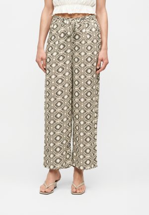 Γυναίκα που φοράει παντελόνες με μπεζ και μαύρα γεωμετρικά ανθικά μοτίβα και μπεζ σανδάλια με τακούνια και λουράκια.