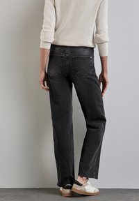 Zwarte rechte jeans met achterzakken, gedragen met een lichtbeige trui en twee-tint schoenen met zwarte en roomkleurige accenten.