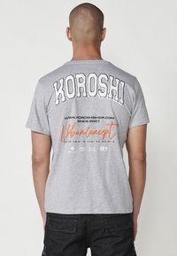 Gray cotton t-shirt featuring bold black "KOROSHI" lettering on the back, orange "Urban Concept," and various printed details.