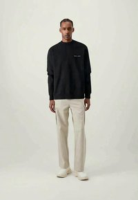 Felpa nera con maniche lunghe e girocollo, abbinata a pantaloni dritti beige chiaro e sneakers bianche. Design minimale.