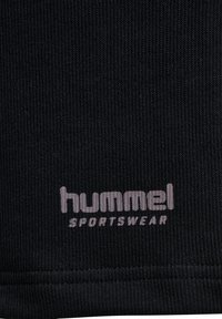 Tissu de sport noir avec texture côtelée, comportant le logo "hummel" en gris clair, positionné vers le bas.