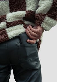 Brown and white checkered fleece jacket paired with fitted black leather pants. The hand is positioned near a back pocket.