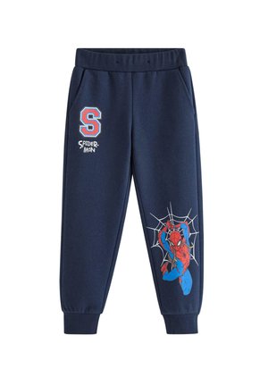 Barn med krøllet blondt hår iført en brun beanie og marineblå Spider-Man træningsdragt, smilende og lænende fremad på en hvid baggrund.